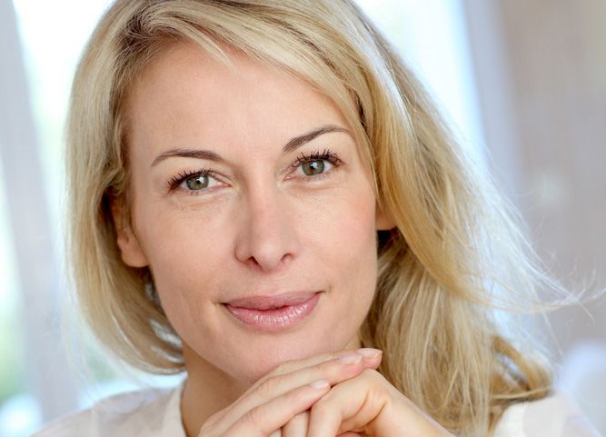 Smiling blond woman holding hands clasped in front of chin